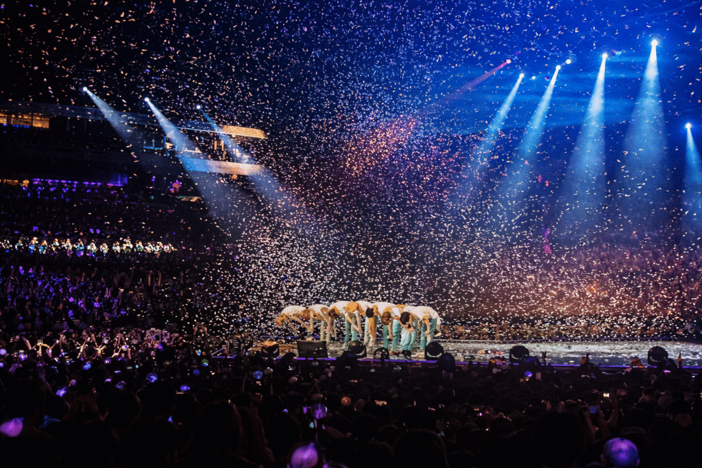 Large stadium concert with performers bowing under confetti and audience lights